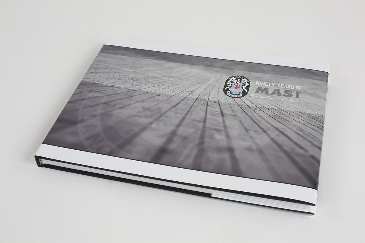 A closed hardcover book titled 90 YEARS OF MASI by Masi Bikes rests on a light surface, featuring a black and white geometric cover with a lions head logo, embodying Cicli Masis storied legacy in European bicycle racing.