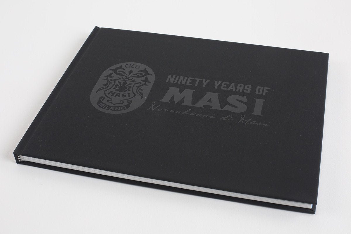 The black hardcover book 90 YEARS OF MASI by Masi Bikes, with silver lettering and a decorative emblem, delves into Cicli Masis cycling history. The cover also includes the Italian phrase Novantanni di Masi, reflecting European bicycle racing heritage.