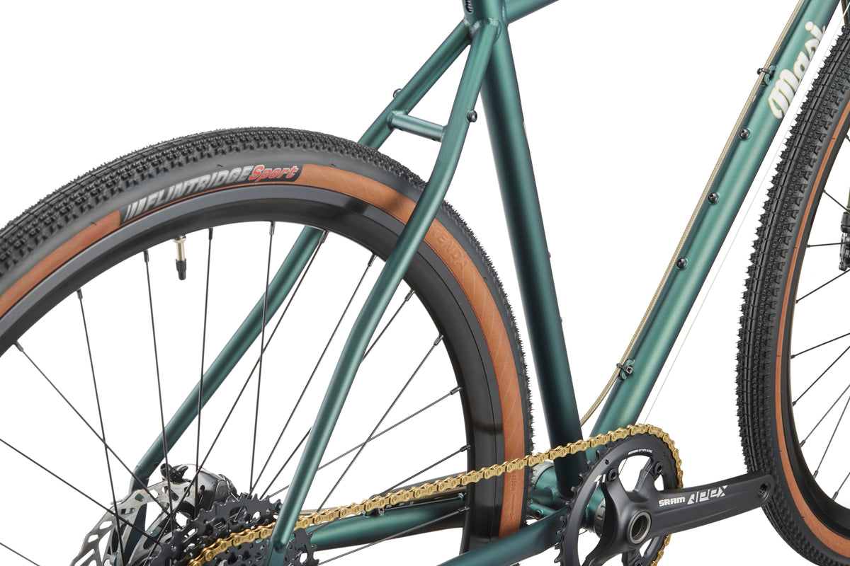 Close-up of CATALINA 1 chromoly steel green frame with tan-walled tires, black crankset, and gold bike chain.