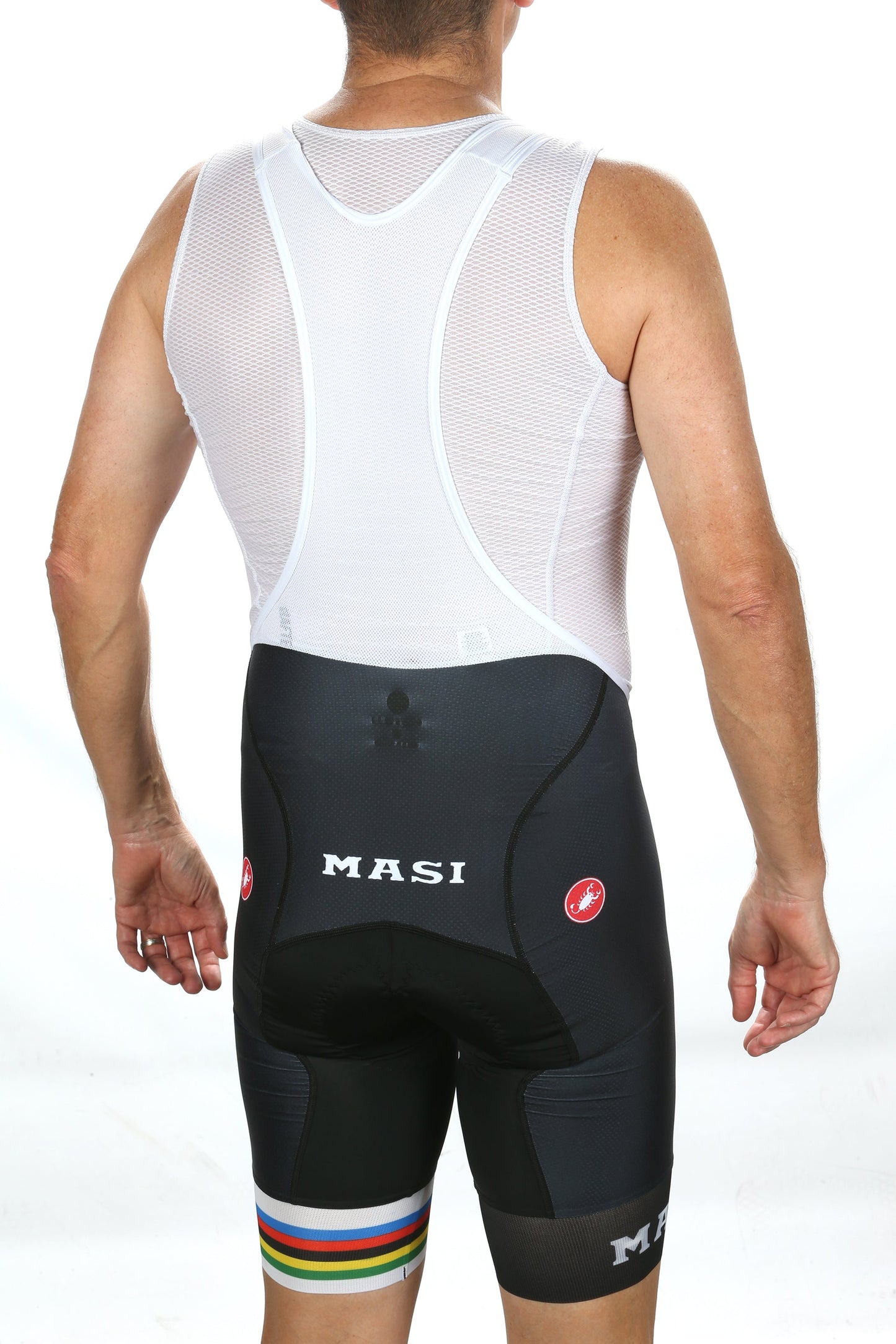 A person stands facing away in a white mesh athletic top and black MASI LEGACY BIBS, featuring rainbow stripes. Masi Bikes is prominently displayed on the shorts, set against a plain white backdrop.