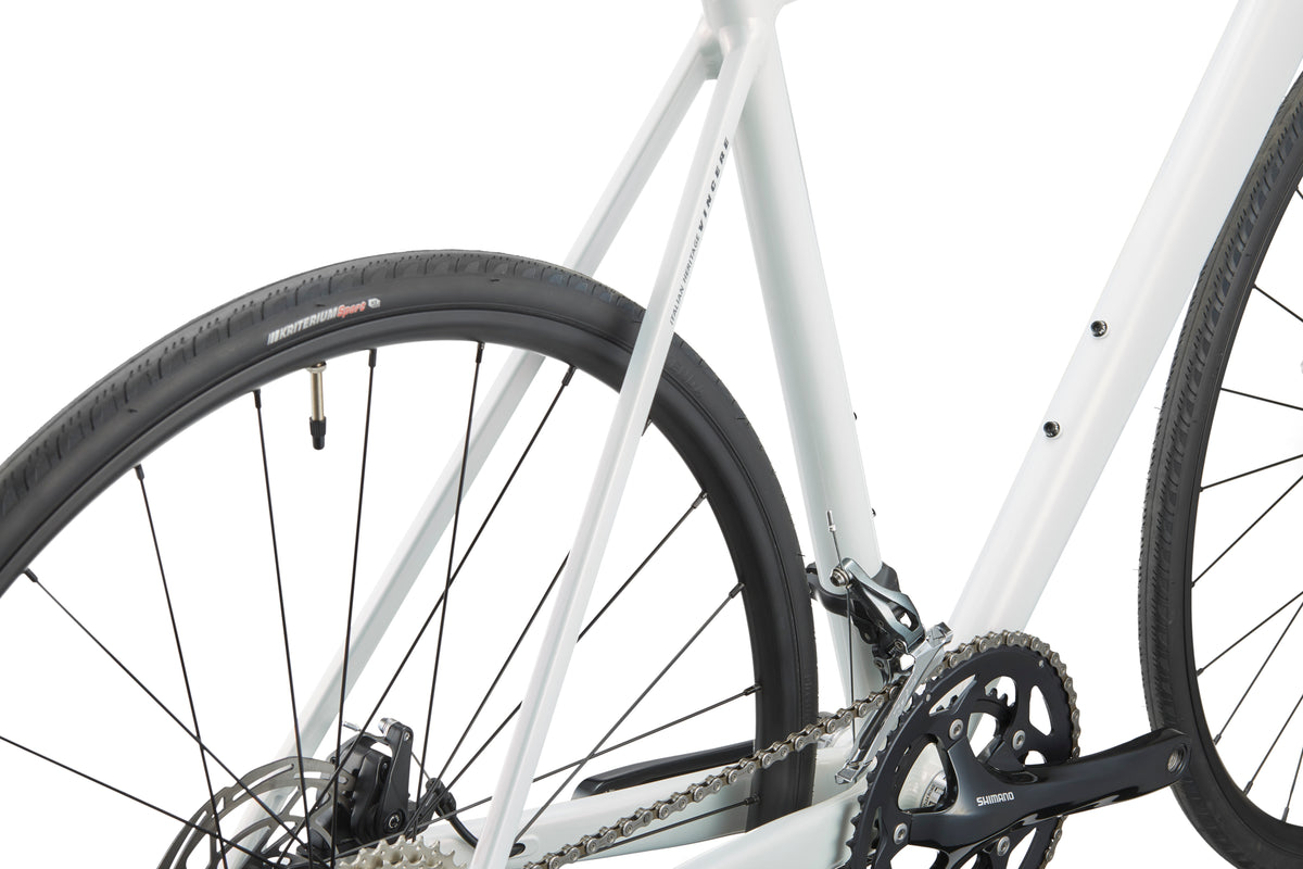 Close-up of a VINCERE 3 bike, highlighting its sleek white alloy frame, rear wheel, and Shimano Tiagra gear mechanism.