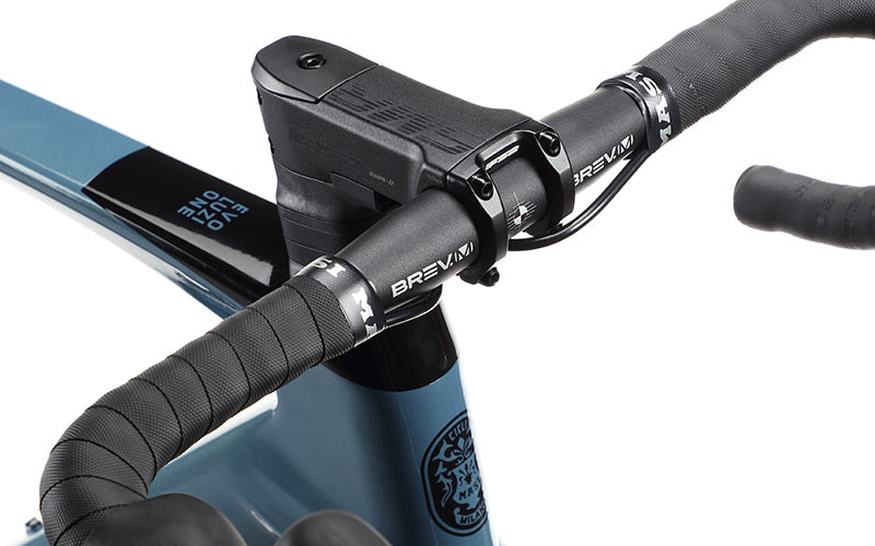 Close-up of a black and blue bicycles handlebar. The handlebar features a sleek design with the brand name Brevani visible. The background shows part of the bikes frame in blue, with a logo and text that reads Evo One.