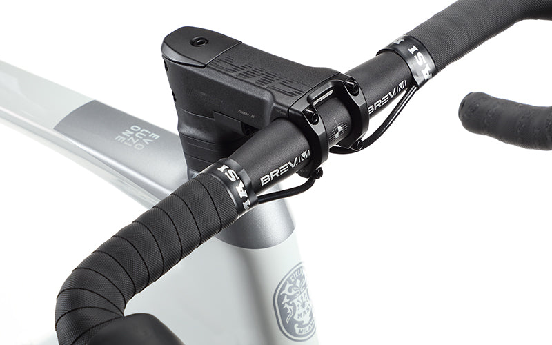 Close-up of EVOLUZIONE 1s handlebars wrapped in black grip tape and a sleek black stem branded Bravia. Partially visible Masi Bikes carbon frame showcases its aerodynamic design with logo and text.