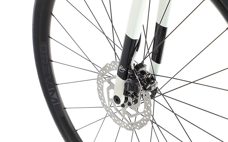 Close-up of VINCERE 4 by Masi Bikes: A bicycle wheel featuring a disc brake system, with a white carbon fork and black accents complementing the alloy frame. The silver brake rotor, thin black spokes, black-rimmed tires, and internal cable routing create a sleek look.
