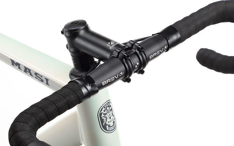 Close-up of a bicycle handlebar with black tape and a BREV M logo. The VINCERE 4 by Masi Bikes showcases an alloy frame in white, adorned with the MASI logo and a crest. Its internal cable routing ensures a sleek design against the plain white background.