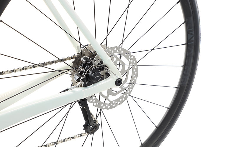 Close-up of the VINCERE 4 by Masi Bikes, featuring its rear wheel with spokes, disc brake, and chain on a sleek white alloy frame. The black tire contrasts against a white background, highlighting the mechanical details and internal cable routing for a streamlined look.