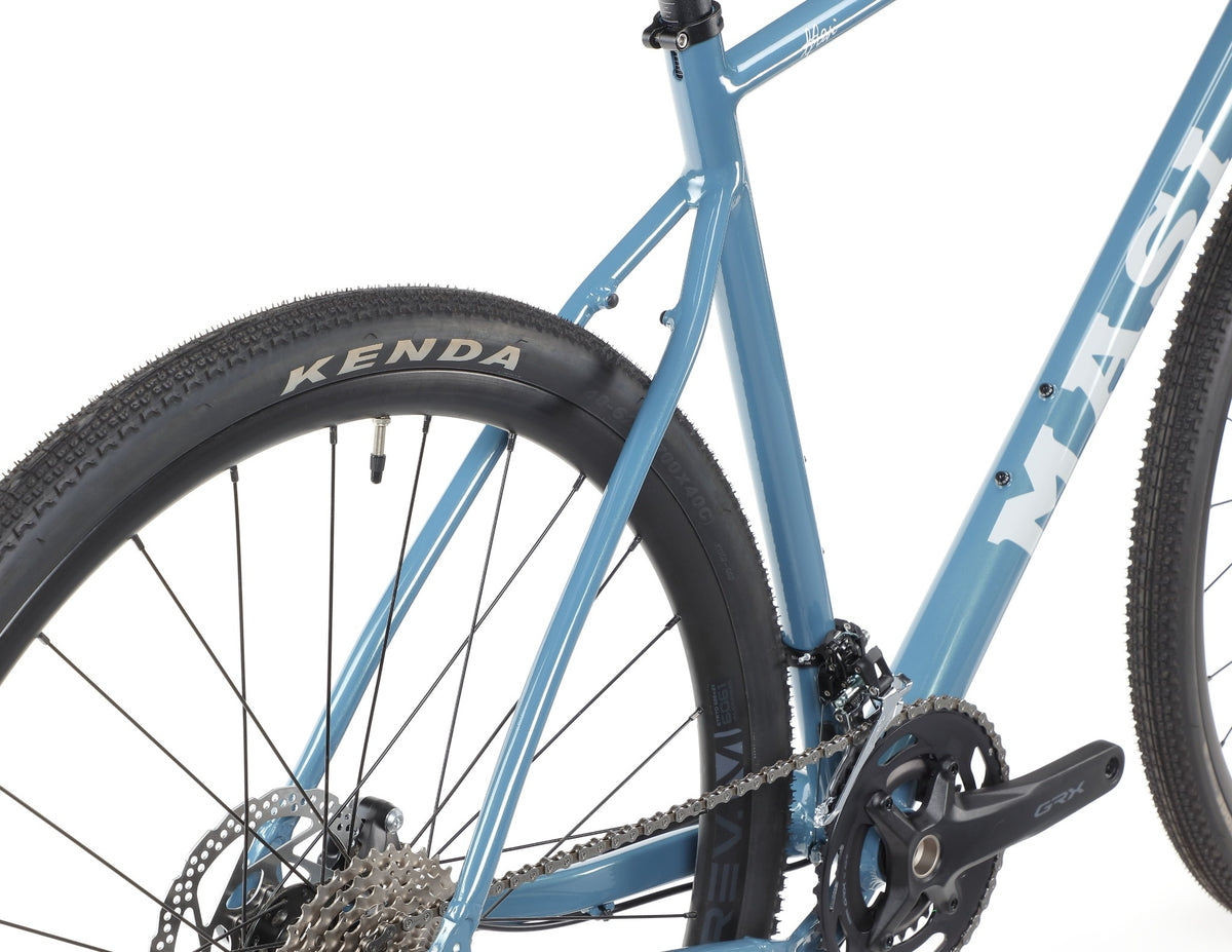 Close-up of BRUNELLO 1’s blue rear wheel, chain, and pedal with KENDA branding and tubeless-ready wheels on white background.