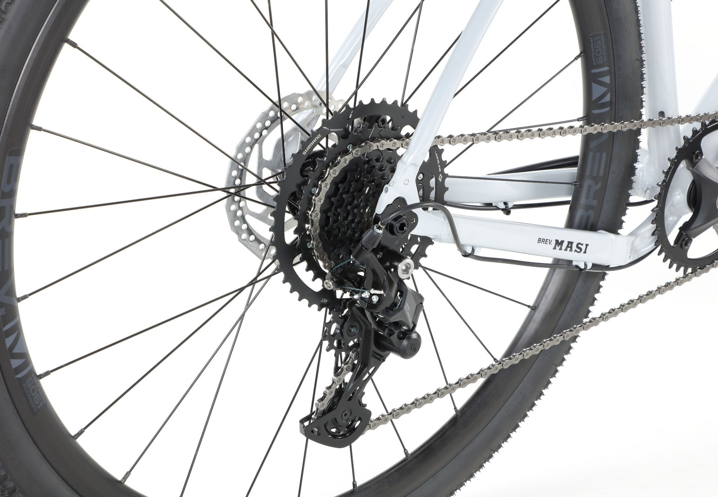 Close-up of BRUNELLO 3 gravel bike’s rear wheel, gears, and derailleur against a white background.