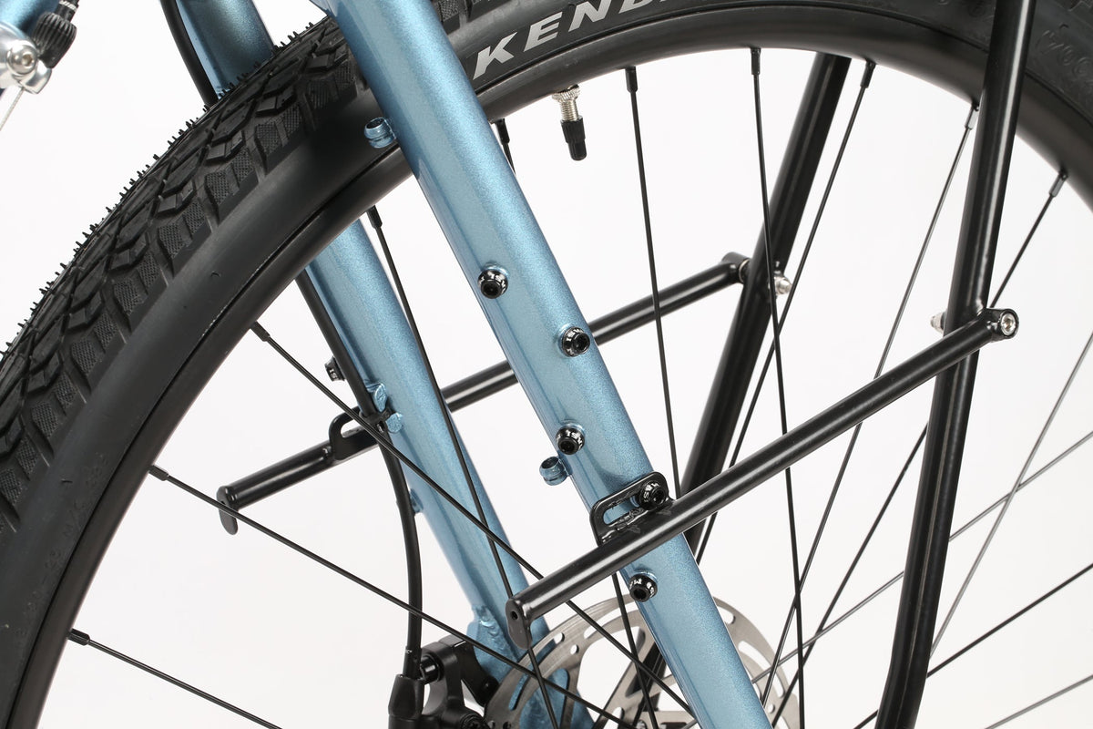 Close-up of the GIRAMONDO 700c by Masi Bikes featuring a light blue metallic frame, black KENDA tire, spokes, and a metal rack mount for adventure. The bike stands against a plain white background.
