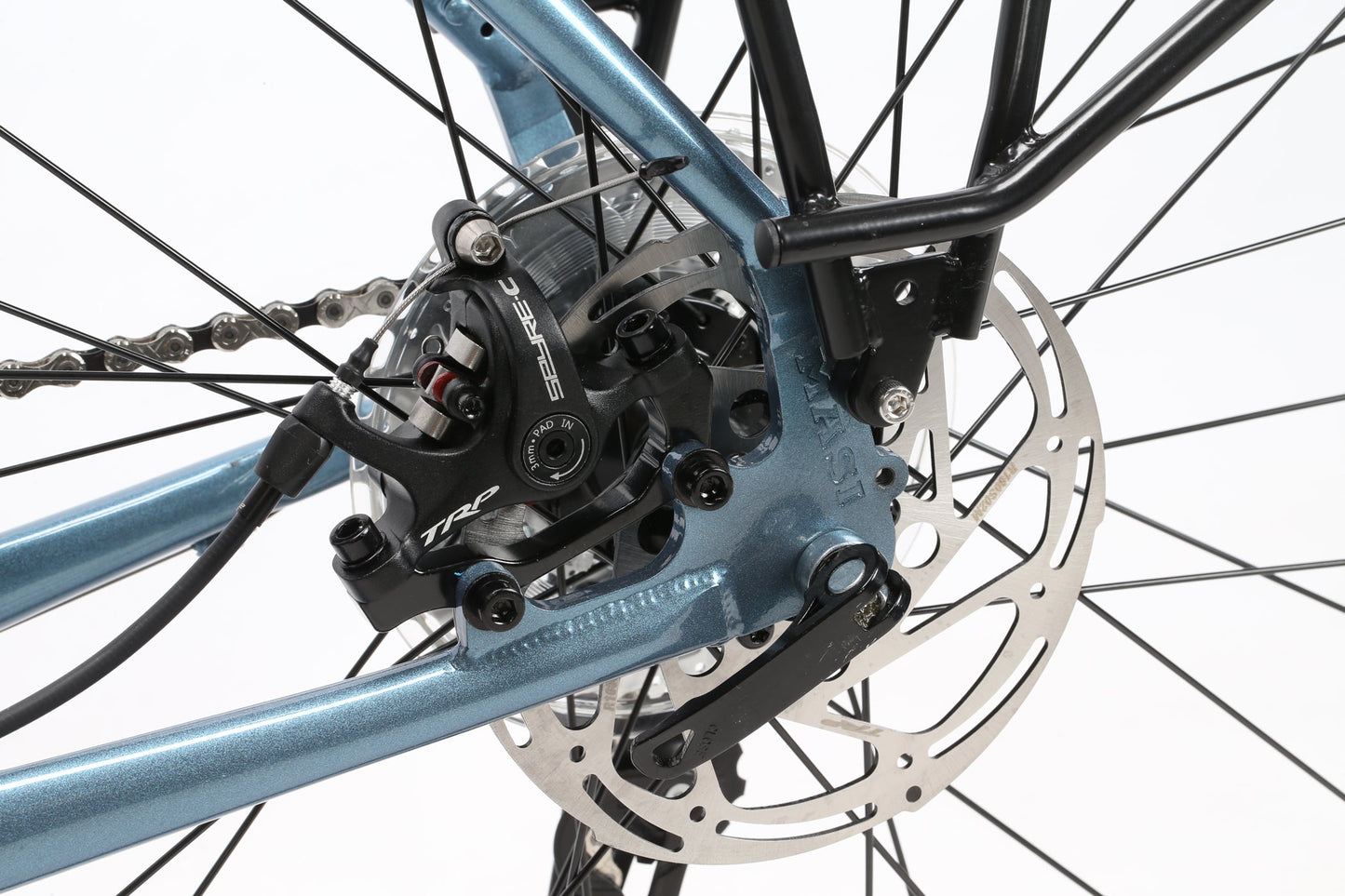 Close-up of Masi Bikes GIRAMONDO 700c rear disc brake system: shiny metallic rotor and black caliper on a blue touring frame, with spokes radiating outward. The chain and gear components, perfect for adventure rides, are partially visible.