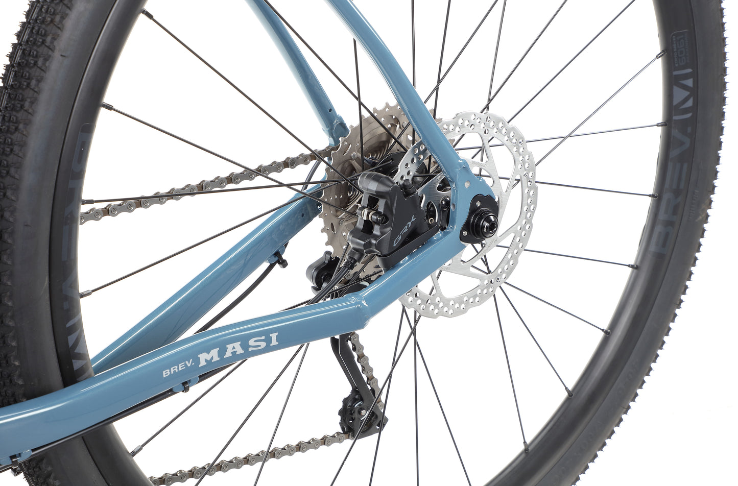 Close-up of a blue BRUNELLO 1 bicycles rear wheel with disc brake, chain, BREV MASI frame label, and a knobby tire.