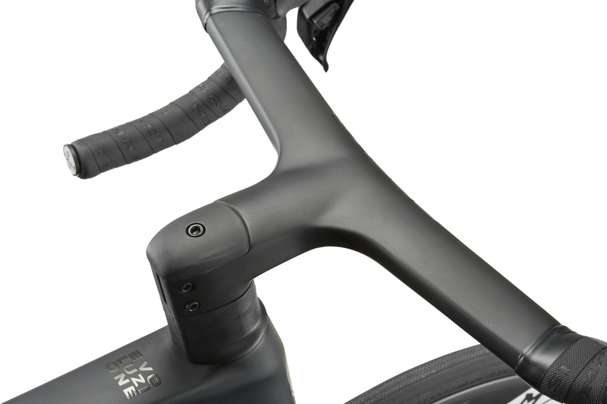 Close-up of a dark gray handlebar and stem on the EVOLUZIONE 1, with textured grips and part of an aerodynamic tire.