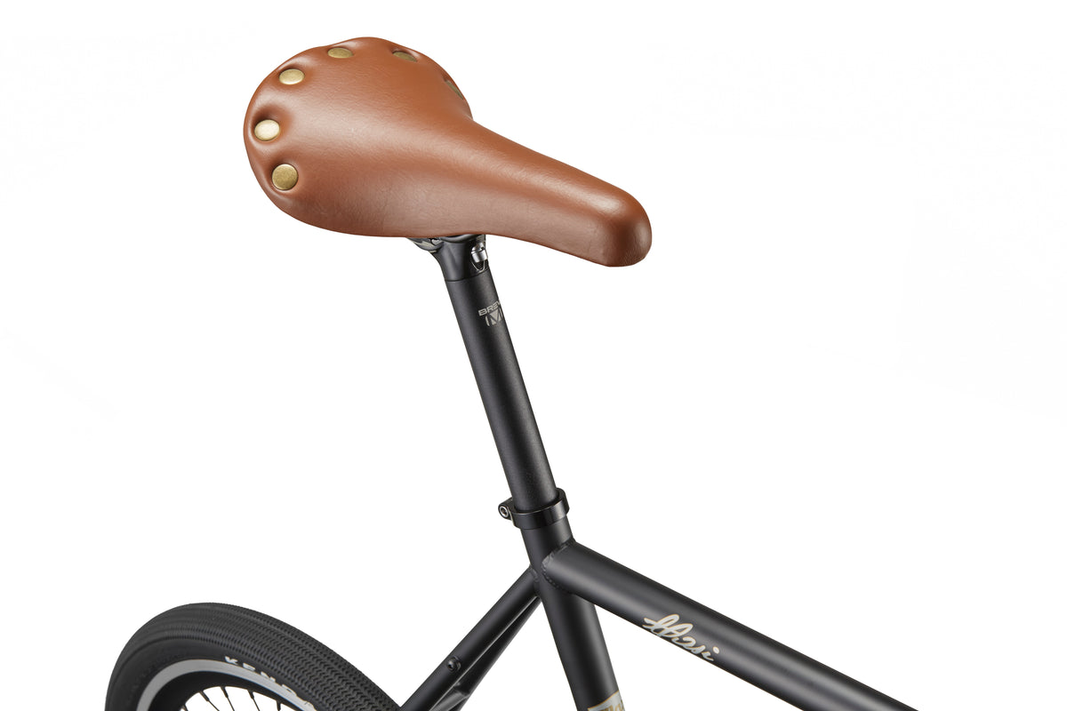 Close-up of a brown leather seat with brass rivets on the STELVIO 3 MiniVelo, highlighting urban style against a white backdrop.