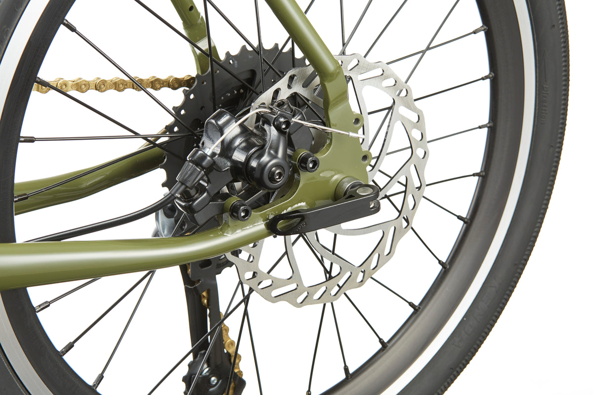 Close-up of STELVIO 2 MiniVelo rear wheel with disc brake, gear cassette, and chain on an olive green urban frame.