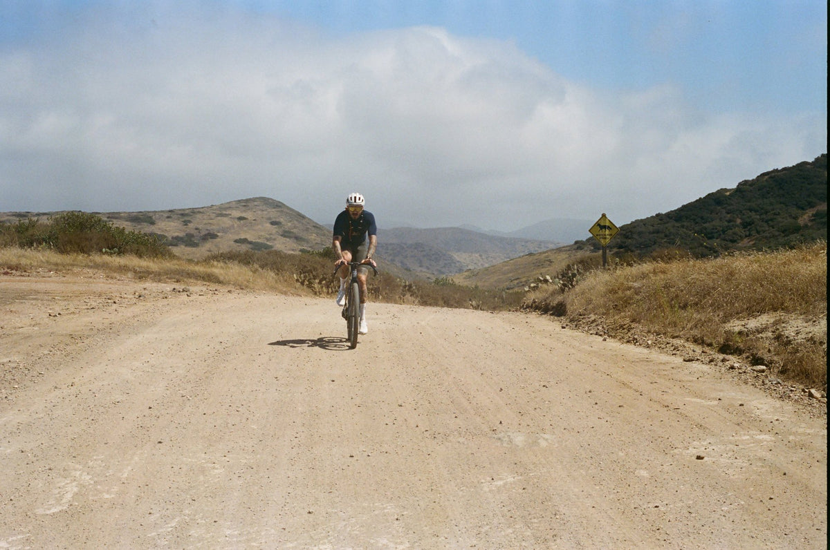 A rider alone on an Oltre Strada, climbing a wide dirt road under open sky