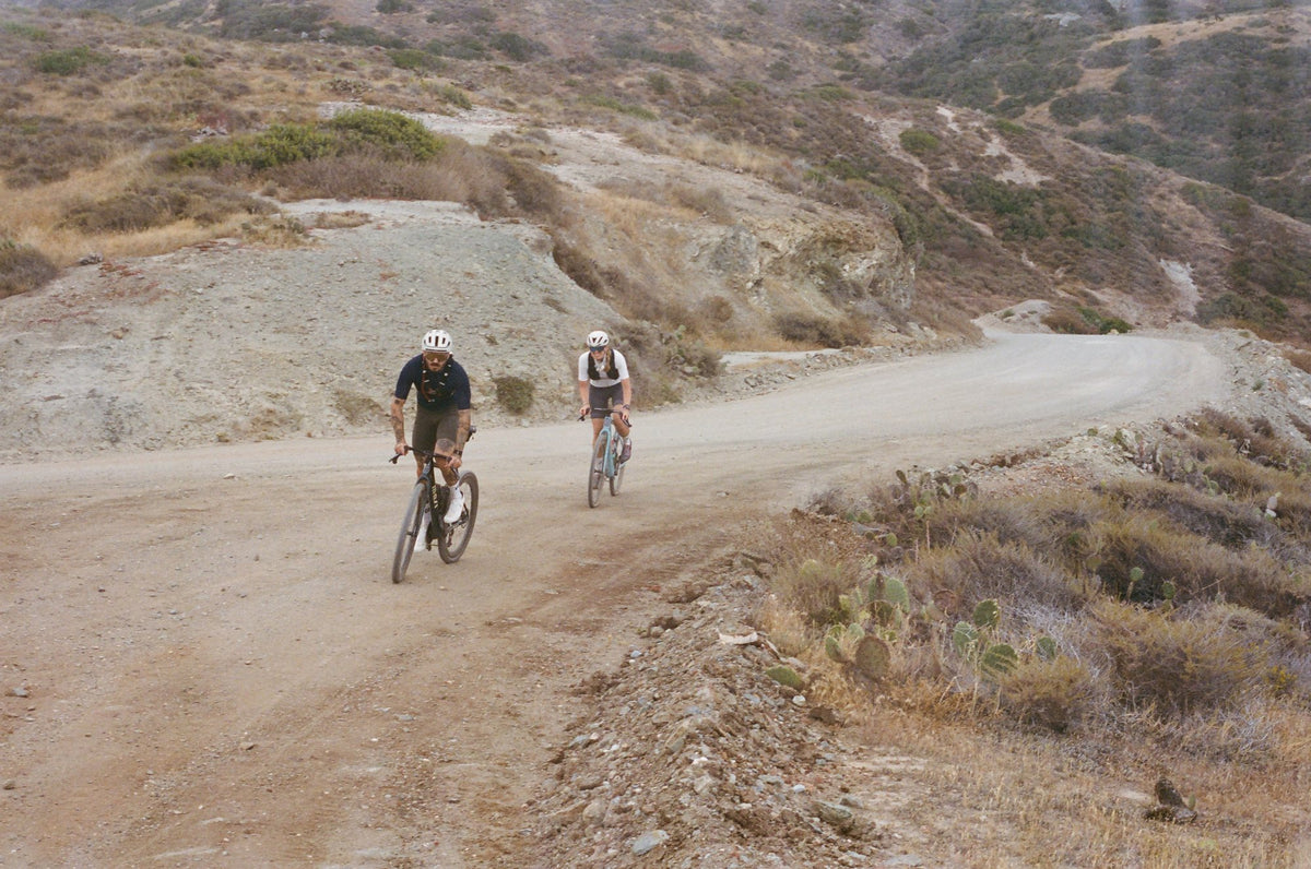 Two riders on Oltre Stradas on a gravel road cut through dry hills