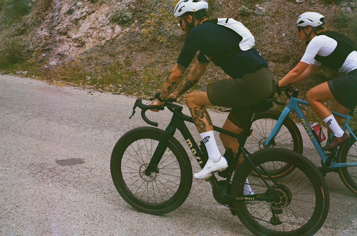 Two riders on Oltre Stradas climbing a paved road, seen from behind