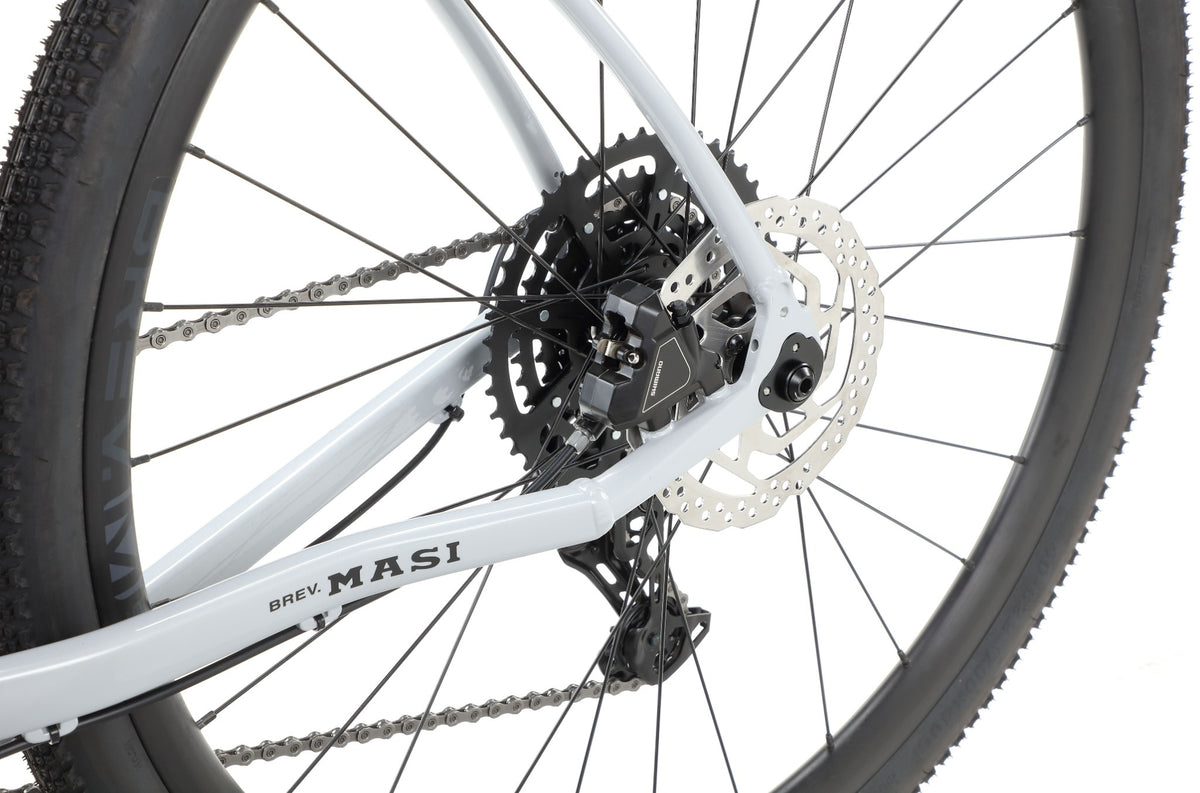 Close-up of the BRUNELLO 3 gravel bike’s rear wheel with disc brake, gears, chain, and BREV. MASI on the alloy frame.