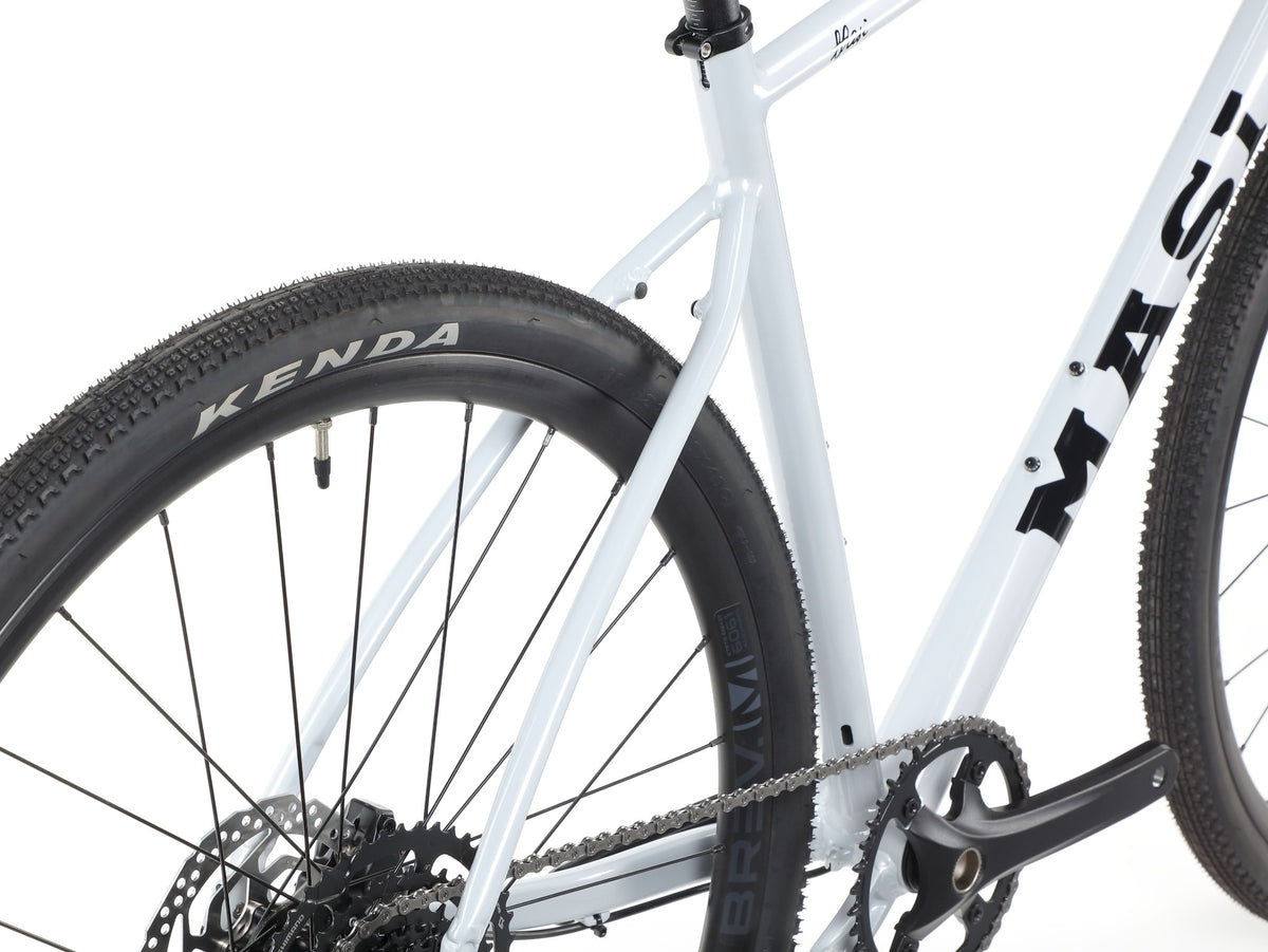 Close-up of BRUNELLO 3s lightweight alloy frame, rear tubeless-ready KENDA tire, chain, and crankset on white background.