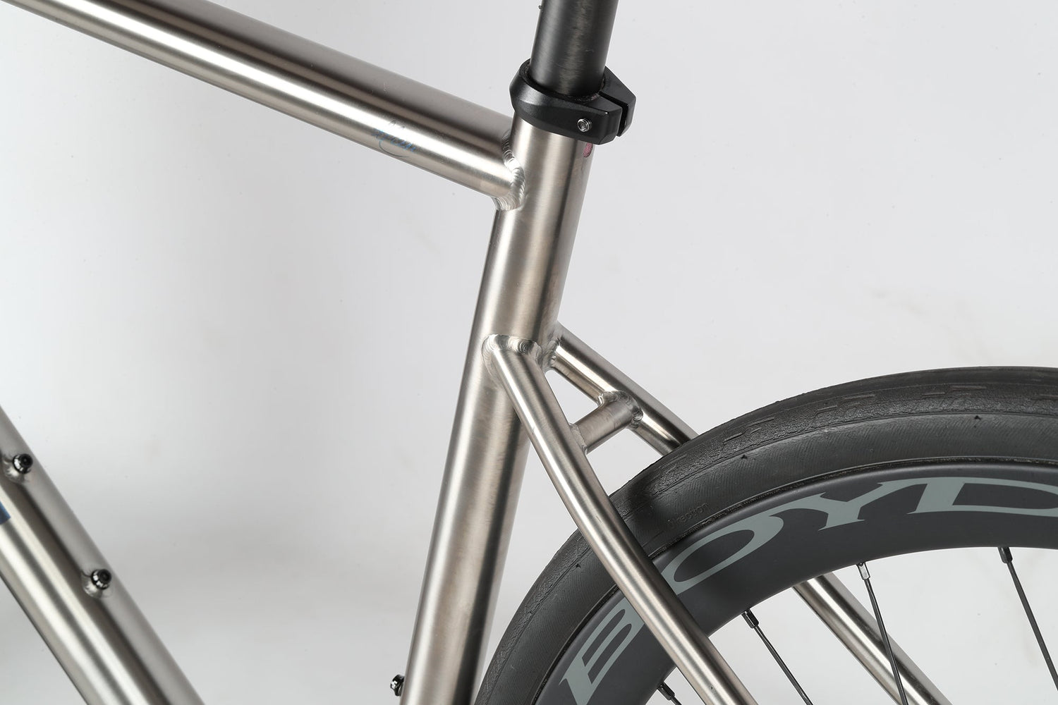 Close-up view of a sleek, metallic bicycle frame featuring a rear wheel with the word BOYD on the tire. The frame showcases smooth welds and a brushed finish, highlighting modern engineering and design.