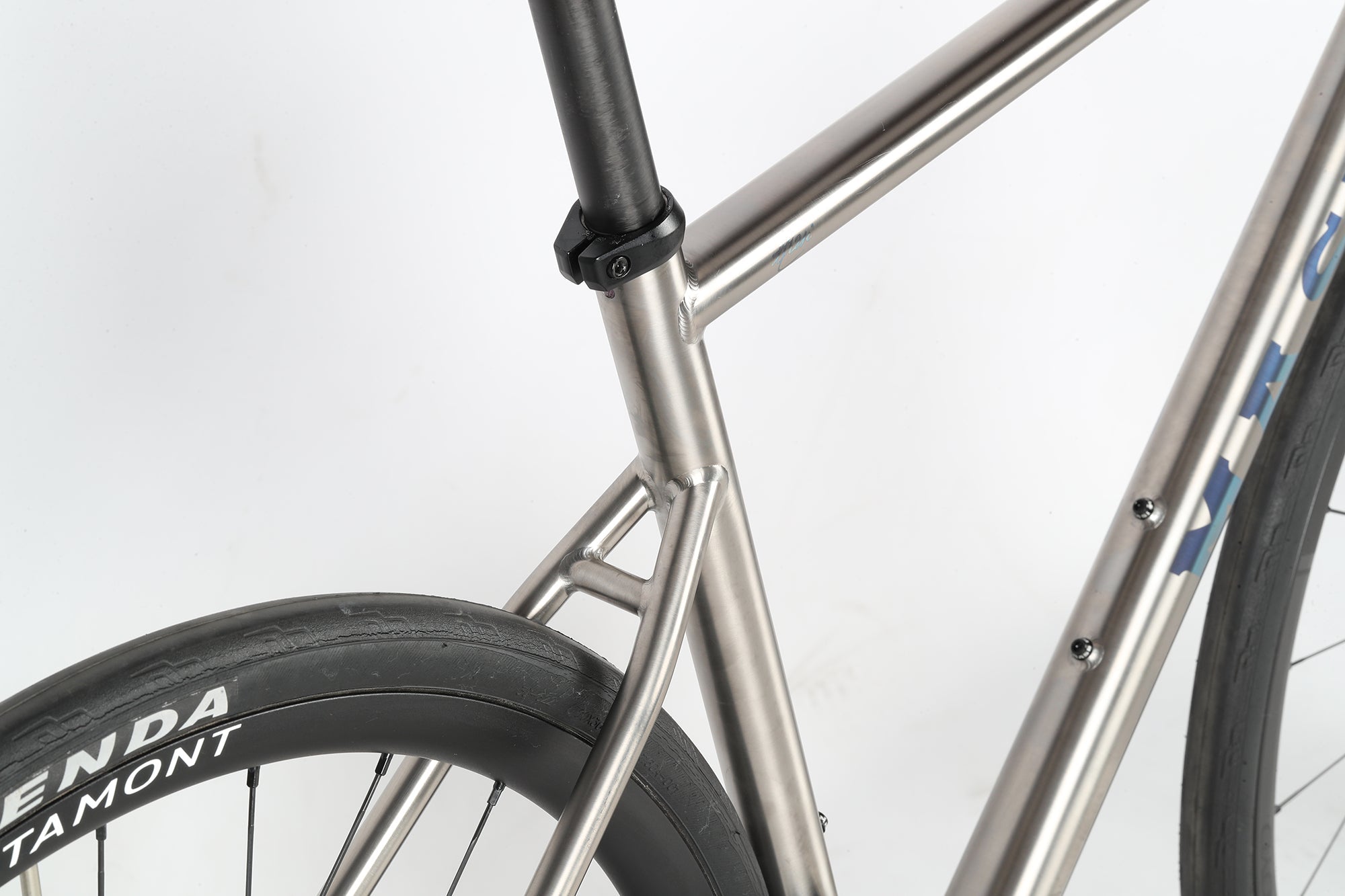 Close-up of a bicycle showing the rear section. The sleek metal frame has a polished finish, and the tire is branded KENDA. The image highlights the bikes clean design and sturdy construction against a plain background.