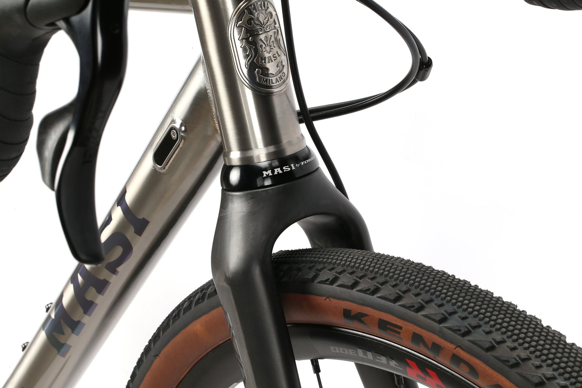 Close-up of the INCANTO CAMPY EKAR Ti bikes front fork and Kenda tire with textured tread. It features a metallic Masi Bikes frame, Campagnolo EKAR 13-speed shifting, and a badge on the titanium part of the frame.