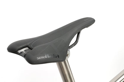 A close-up of a Masi Bikes INCANTO CAMPY EKAR Ti saddle in black, featuring a Titanium rail and mounted on a metal seat post against a white background. The design is sleek and aerodynamic with subtle perforations for ventilation.