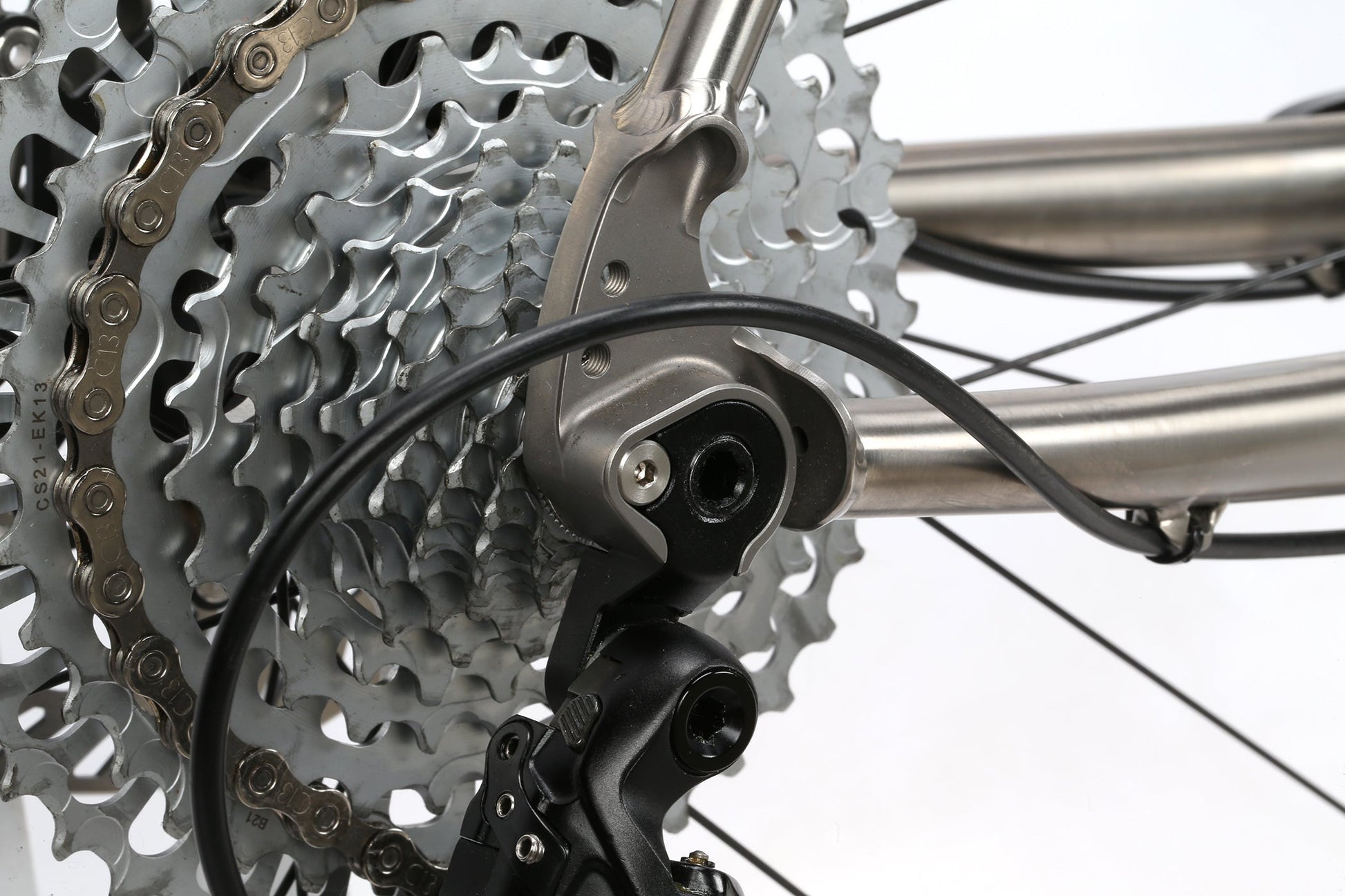 Close-up of the INCANTO CAMPY EKAR Ti 13-speed rear derailleur and cassette by Masi Bikes, showcasing titanium components against bicycle spokes. The drivetrain’s details are highlighted with a black cable connected to the derailleur.